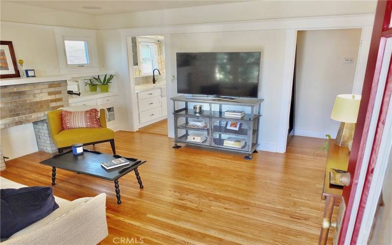 Inviting living room adorned with beautiful wood flooring, elegant picture rail molding, and windows that fill the space with natural light. Charming built-in cabinets are nestled where the old fireplace once graced the room