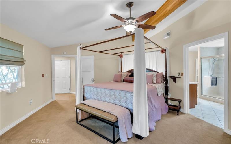 Primary bedroom suite with beamed ceiling, ceiling fan, carpeting, and en suite bathroom.