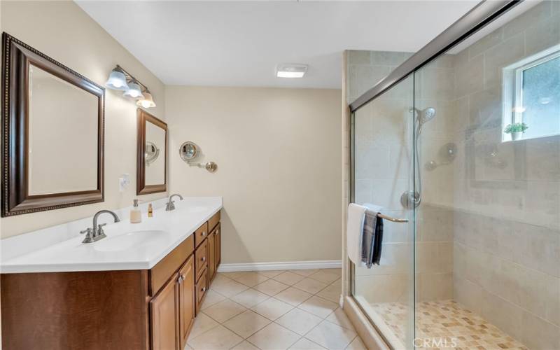 En suite bathroom with dual sinks, large walk-in shower, and tile flooring.