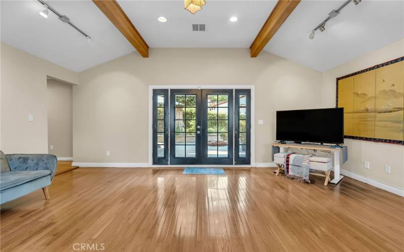 Alternate view from the fireplace of the step-down family room with French doors leading to the private backyard. Hallway to the left leads to the primary bedroom suite.