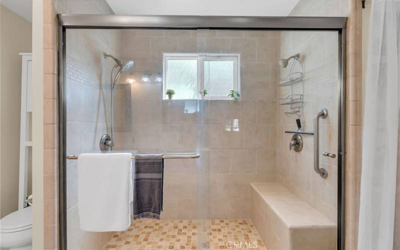 Large shower with dual shower heads and shaving bench.