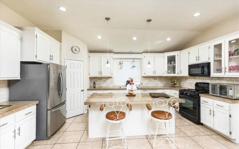 Kitchen with granite counters, walk in pantry, island and custom lighting.  Opens to family room.