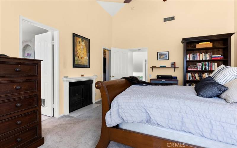 Vaulted ceilings in the primary bedroom.  Note the cozy fireplace as well as arched windows letting in natural light.