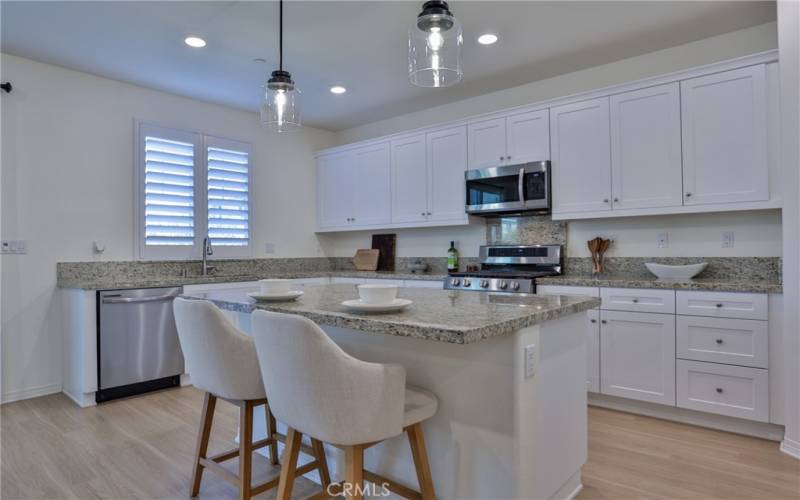 Imagine cooking in this elegant kitchen! Look how bright this kitchen is with the recessed lighting and hanging pendants over the island. Plantation shutters cover a window overlooking the back yard and patio.