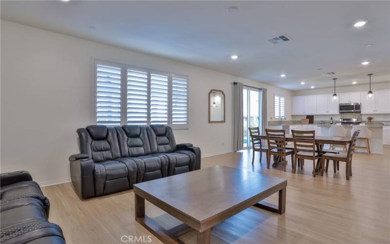 View from living room. Plantation shutters with a view of the back yard/patio and open concept with dining area in between the living and kitchen areas. Recessed lighting in the living/dining/kitchen areas.