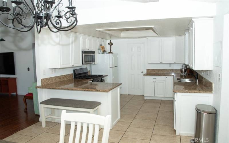 Kitchen with granite counters, modern white cabinets, tile floors, stainless steel appliances, breakfast bar, recessed lighting and pantry.