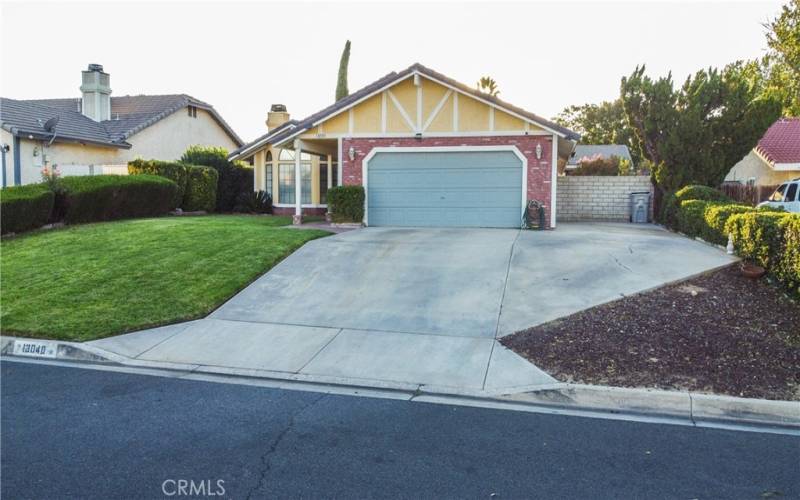 To the right of the home you can see the large concrete pad for potential RV or boat parking.  The picture also highlights the front of the home showing grass and mature landscaping as well as brick walk way under the covered entry.  There is a tile roof and brick facade and the front door and garage are painted to match.