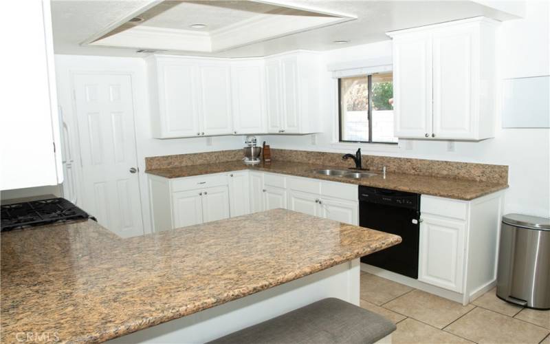 Kitchen with granite counters, modern white cabinets, tile floors, stainless steel appliances, breakfast bar, recessed lighting and pantry.