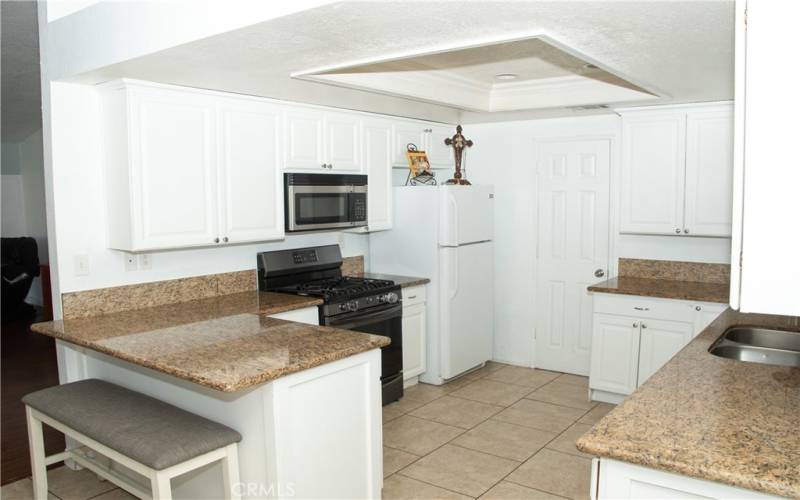 Kitchen with granite counters, modern white cabinets, tile floors, stainless steel appliances, breakfast bar, recessed lighting and pantry.