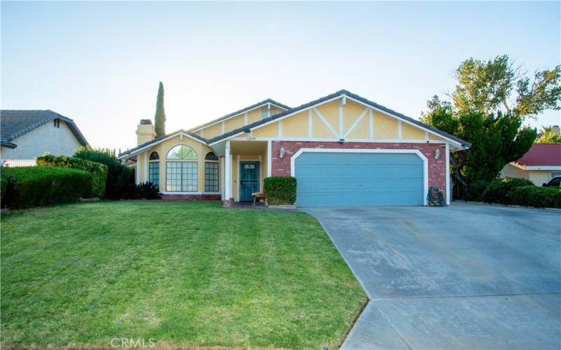 The front of the home showing grass and mature landscaping as well as brick walk way under the covered entry.  There is a tile roof and brick facade and the front door and garage are painted to match.