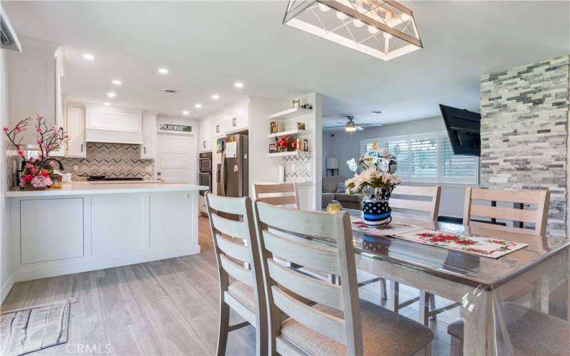 This is a picture of the dining room in the house. The dining room has a view of the kitchen. The dining room is spacious and has a large window that lets in lots of natural light.