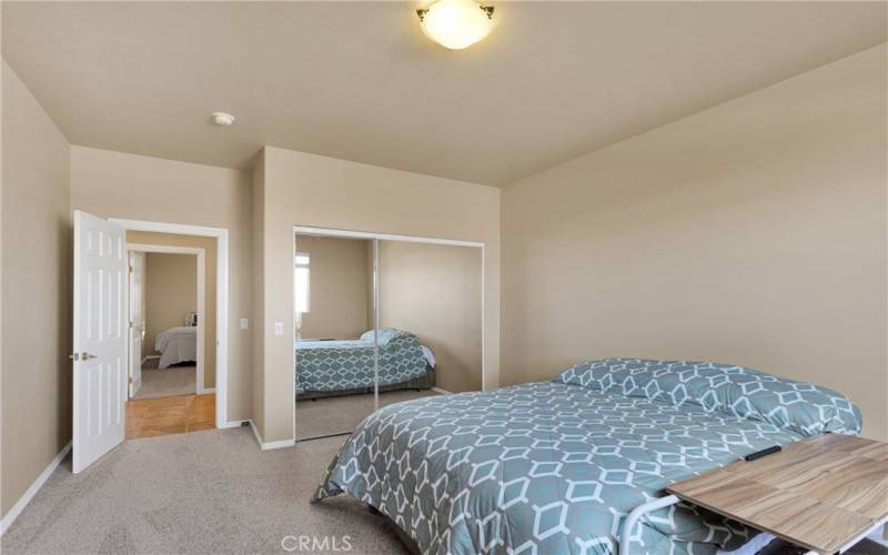 Large hall bedroom with mirrored closet doors, neutral paint, fraise carpeting, and high ceilings.