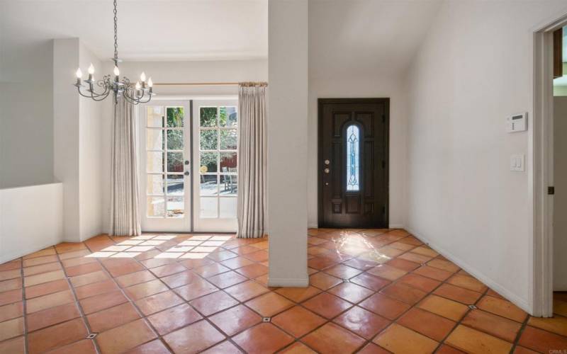 w/ hanging chandelier. Terracotta-tiled flooring,  Natural light filtering from the double doors,