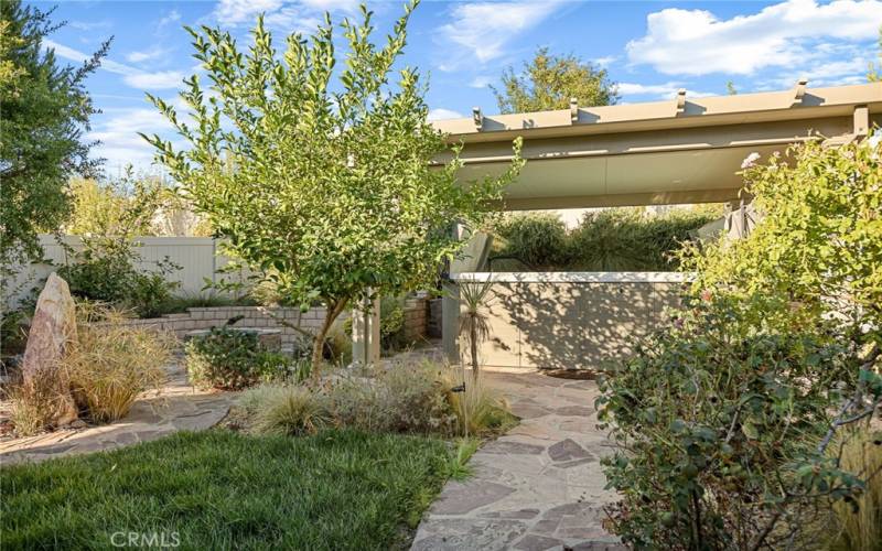 Backyard with tall rock water fountain on left, on right slate path to Pergola with Swim Spa