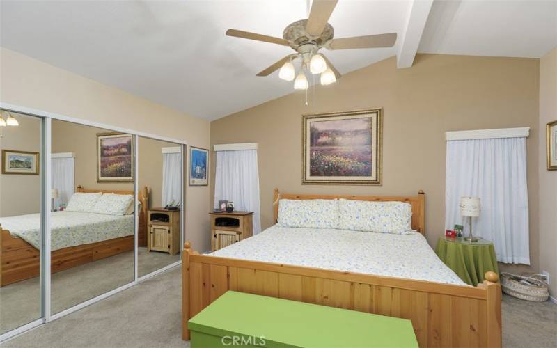 The grand master bedroom has a wall of closets with mirrored doors, soaring ceilings and ceiling fan.