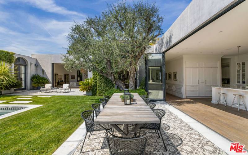 Beautiful seamless indoor/outdoor 'Nanawall' doors throughout the home. Image of outdoor dining area with 100 year old olive tree facing north.