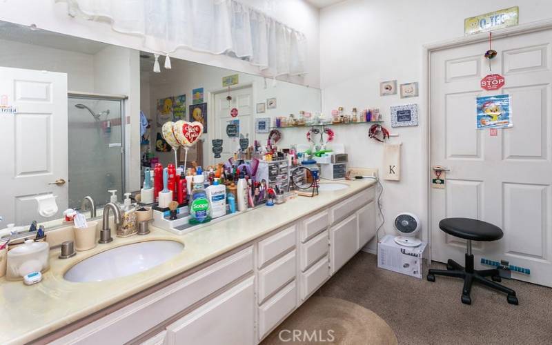 Primary en suite bathroom with oversized vanity, dual undermount basins, and a glass-enclosed tub/shower.