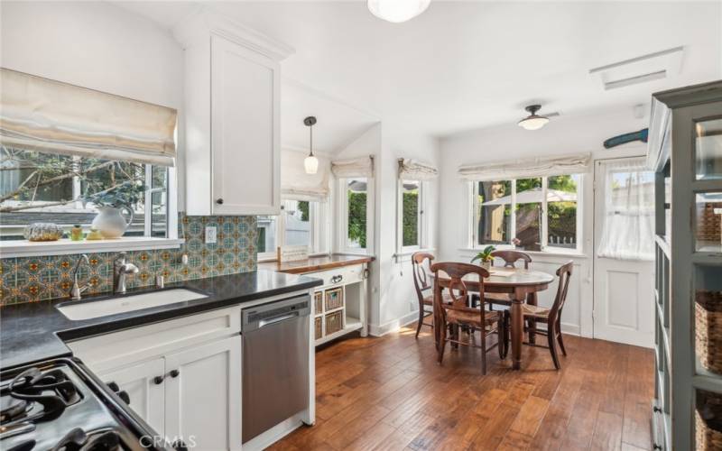  Offering garden views, the kitchen presents a dining area, solid-surface countertops, white Shaker cabinetry, and stainless steel appliances.