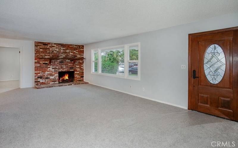 The living room is drenched in natural light from a multitude of windows and is enhanced by a floor-to-ceiling brick fireplace with mantle, and plush new wall-to-wall carpet.