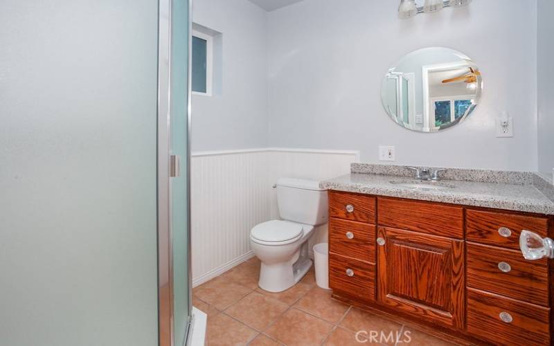 Primary en suite bathroom with vanity, undermount basin, wainscoting, glass-enclosed step-in shower, and tile floors.