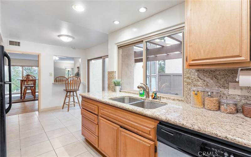 Here you see recessed lighting, kitchen dual pane window that sees the front yard, some of the dining room, dishwasher, sink, drawers, flooring, and breakfast counter.