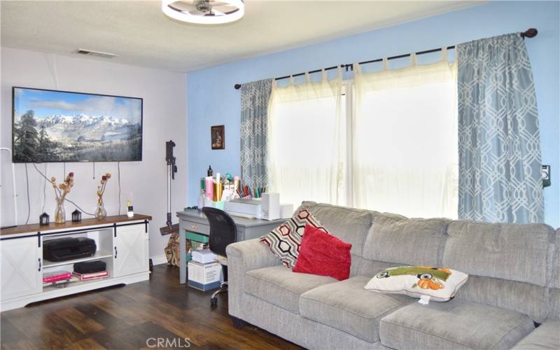 The spacious living room is at the front of the house with windows looking out on the front yard, gorgeous wood laminate flooring, and a modern ceiling fan light.