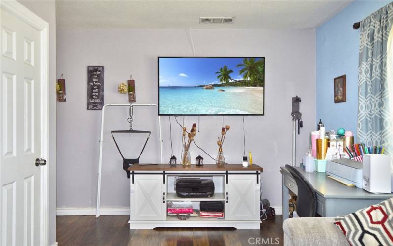 The spacious living room is at the front of the house with windows looking out on the front yard, gorgeous wood laminate flooring, and a modern ceiling fan light.