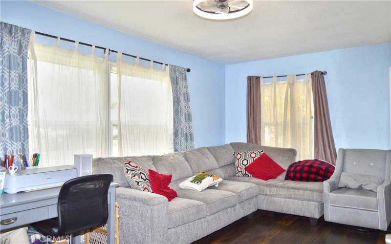 The spacious living room is at the front of the house with windows looking out on the front yard, gorgeous wood laminate flooring, and a modern ceiling fan light.