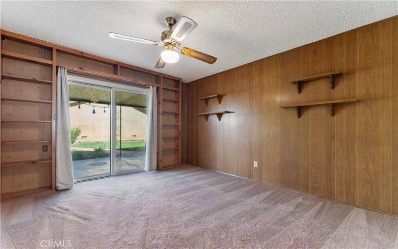 First bedroom on the right side of the hallway between full bath and primary bedroom. Last used as a den. Has sliders to the backyard and custom made shelves.