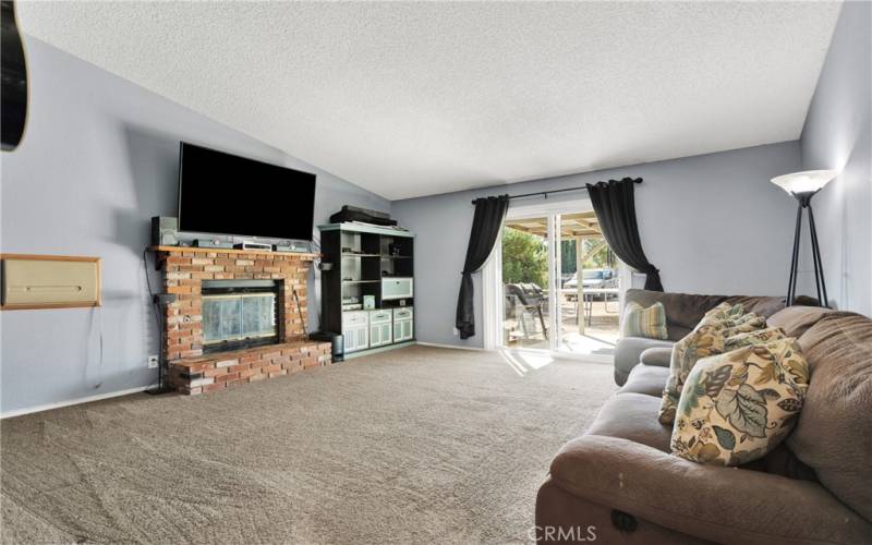 Large living room with raised hearth brick fireplace. Slider leads to large covered patio.