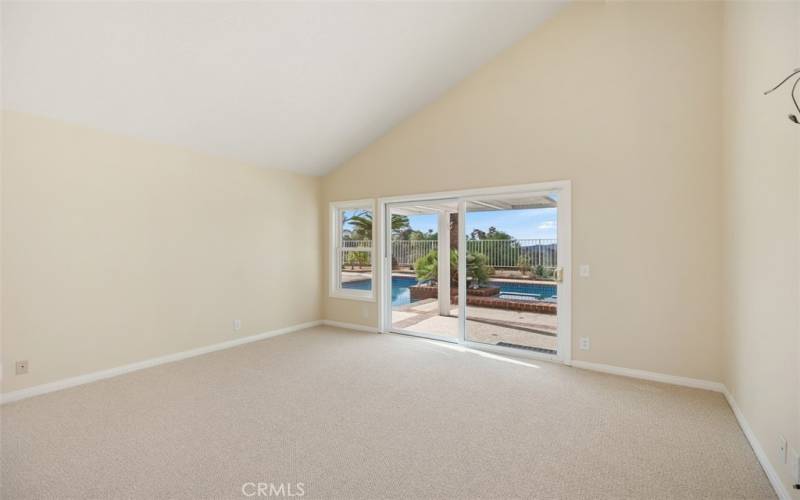 Primary bedroom with vaulted ceilings and door opens to the backyard and pool area.