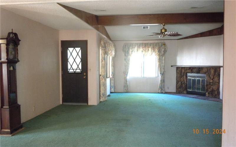 View of the living room from the front door.  Cathedral ceiling with beamed accents, and a wood burning fireplace.  Door in the left of the photo leads to the rear enclosed patio with a spa.