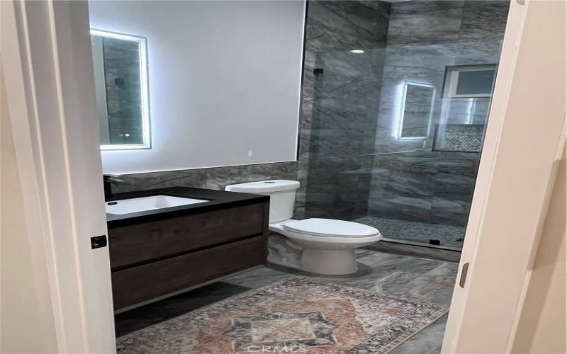 modern design with stunning dark marble tile throughout, creating a spa-like atmosphere. The spacious glass-enclosed shower is fitted with elegant brass fixtures and a stylish herringbone tile accent, blending functionality with high-end finishes.