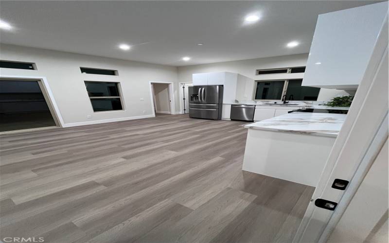 The marble-patterned countertops and ample cabinet space add a touch of elegance, while the wood-style flooring flows seamlessly into the adjacent areas, creating a cohesive living space.