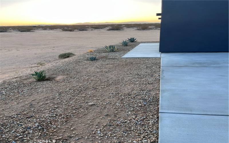 The gravel-lined border with desert succulents adds a touch of greenery that complements the expansive desert landscape beyond the patio.