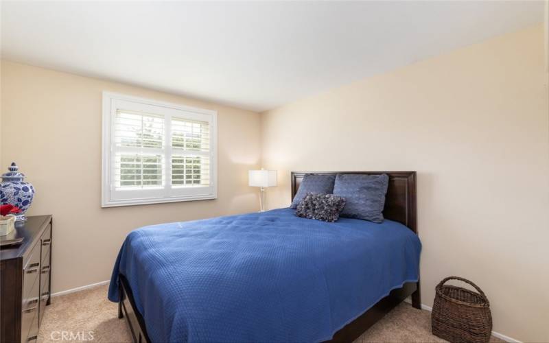 This bedroom has a spacious layout, large windows with plantation shutters, and natural lighting.