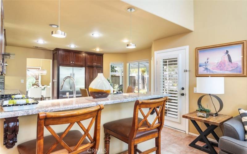 A cozy and inviting kitchen and family room featuring rich wooden cabinetry, modern lighting, and a breakfast bar, seamlessly connecting to the outdoor living space.