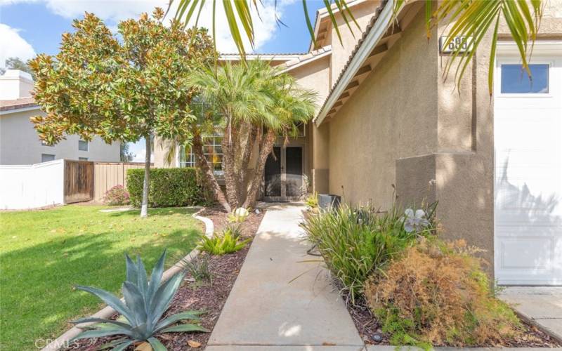 A welcoming walkway lined with vibrant landscaping and tropical palms leads to the inviting entrance of this charming home.