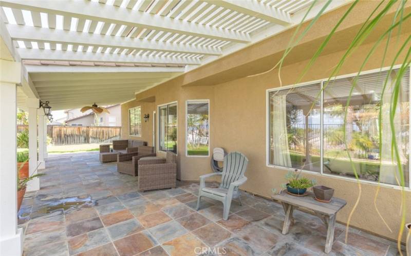 This inviting patio area, shaded by a stylish pergola, features elegant stone flooring and comfortable seating, perfect for enjoying the serene garden views and outdoor relaxation.