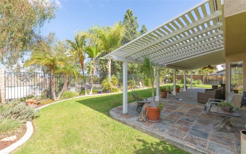 This expansive backyard features a beautifully tiled covered patio, lush greenery, offering a perfect outdoor oasis for relaxation and entertainment.