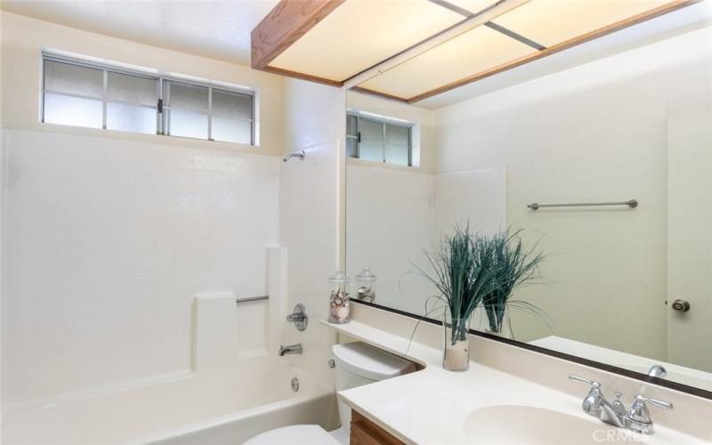 Bright bathroom featuring a shower-tub combo, large mirror, and soft natural light from frosted windows.