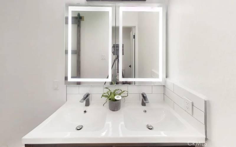 Dual vanities with lighting and dual sinks with storage below.