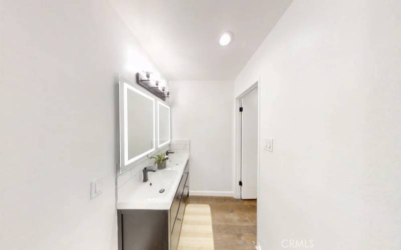 Dual vanities with lighting and dual sinks with storage below. Toilet and shower in door to the right.