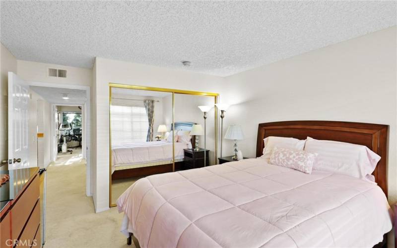 Secondary bedroom #1 with mirrored wardrobe doors looking down hallway toward next bedroom