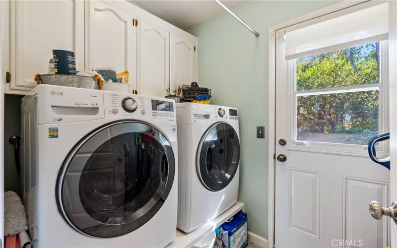 The laundry room offers cabinets above and a door to the outside patio. Washer and dryer stay!