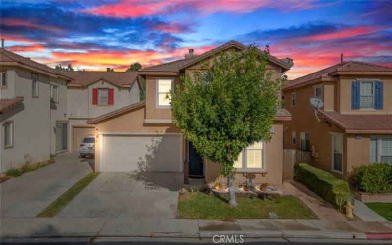 This charming two-story home features a welcoming appearance with a lush front tree, a cozy porch, and a warm exterior, perfect for comfortable family living.