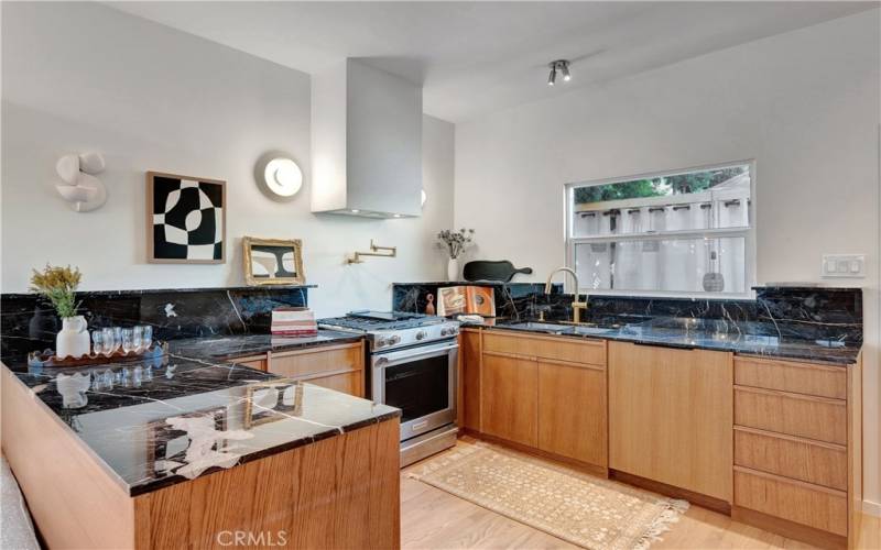 Kitchen with marble countertops, custom minimalist vertical wood-grain cabinets, new stainless range/oven, paneled Bosch dishwasher, and a pot filler below the exterior vented range hood