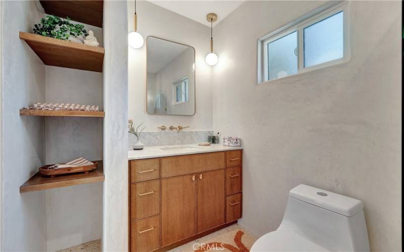 Primary bathroom with marble counter, new vanity, wall mounted faucets and custom shelving