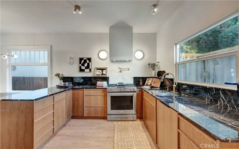 Kitchen area with marble countertops, custom minimalist vertical wood-grain cabinets, new stainless appliances, and paneled Bosch dishwasher