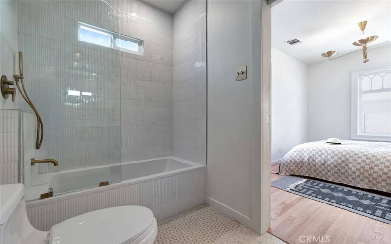 Ensuite bathroom to the bedroom with vertical tile in shower and hex terrazzo tile in floors